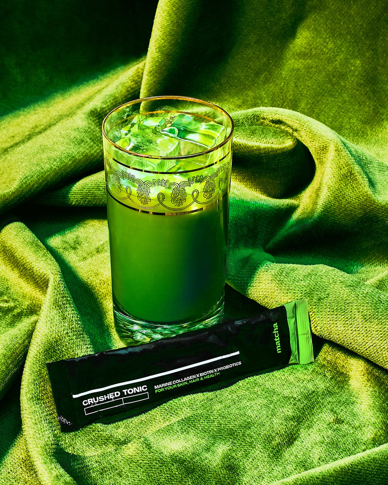 A photo of a stick of Marine CollagenxBiotinxProbiotics Matcha next to a glass with prepared matcha collagen, with a green velvet background